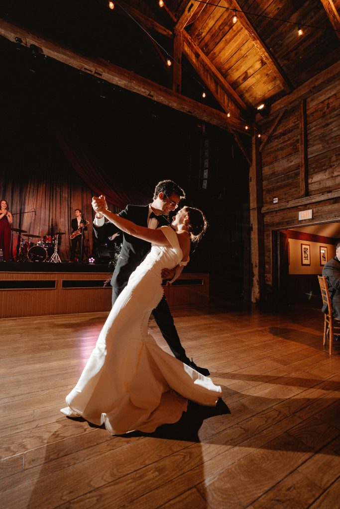 The newlyweds share a dramatic pose during their first dance while the band plays on stage at The Barns at Wolf Trap.  Warm light washes over them.